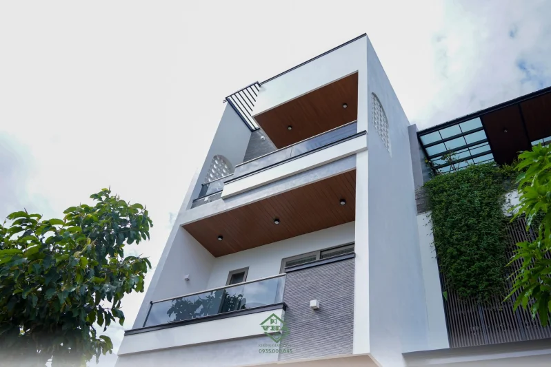 Mặt tiền nhà phố hiện đại 1 trệt 2 lầu với kiến trúc tối giản, ban công kính và hệ lam trang trí tạo điểm nhấn sang trọng.
